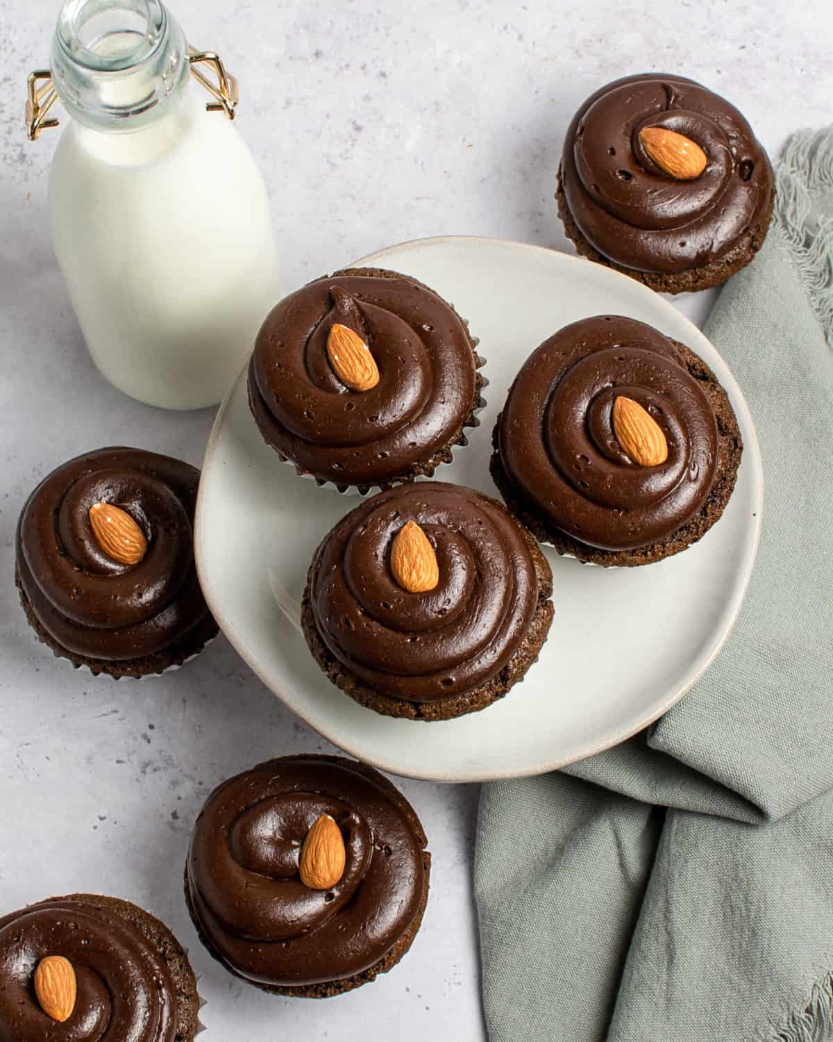 An overhead shot of cupcakes topped with almonds and a glass of milk.