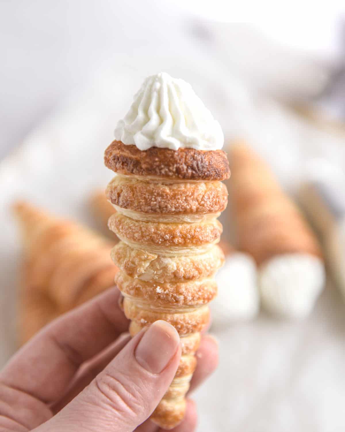 A close up of a hand holding a single cream horn.