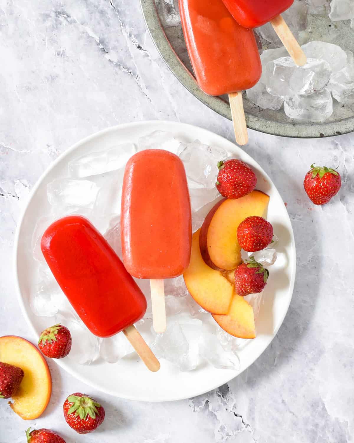 Mexican popsicles on ice surrounded with fresh strawberries and peaches.