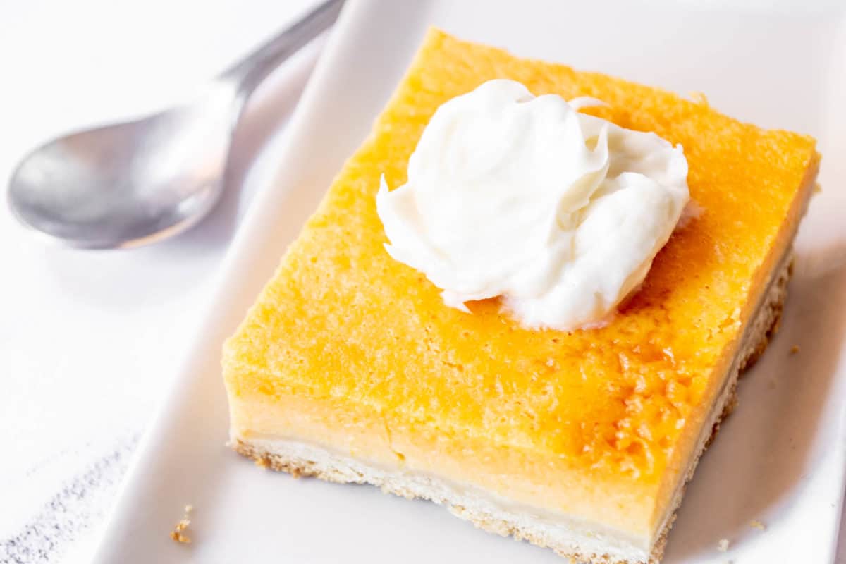 A square pumpkin pie bar on a plate topped with whipped cream.