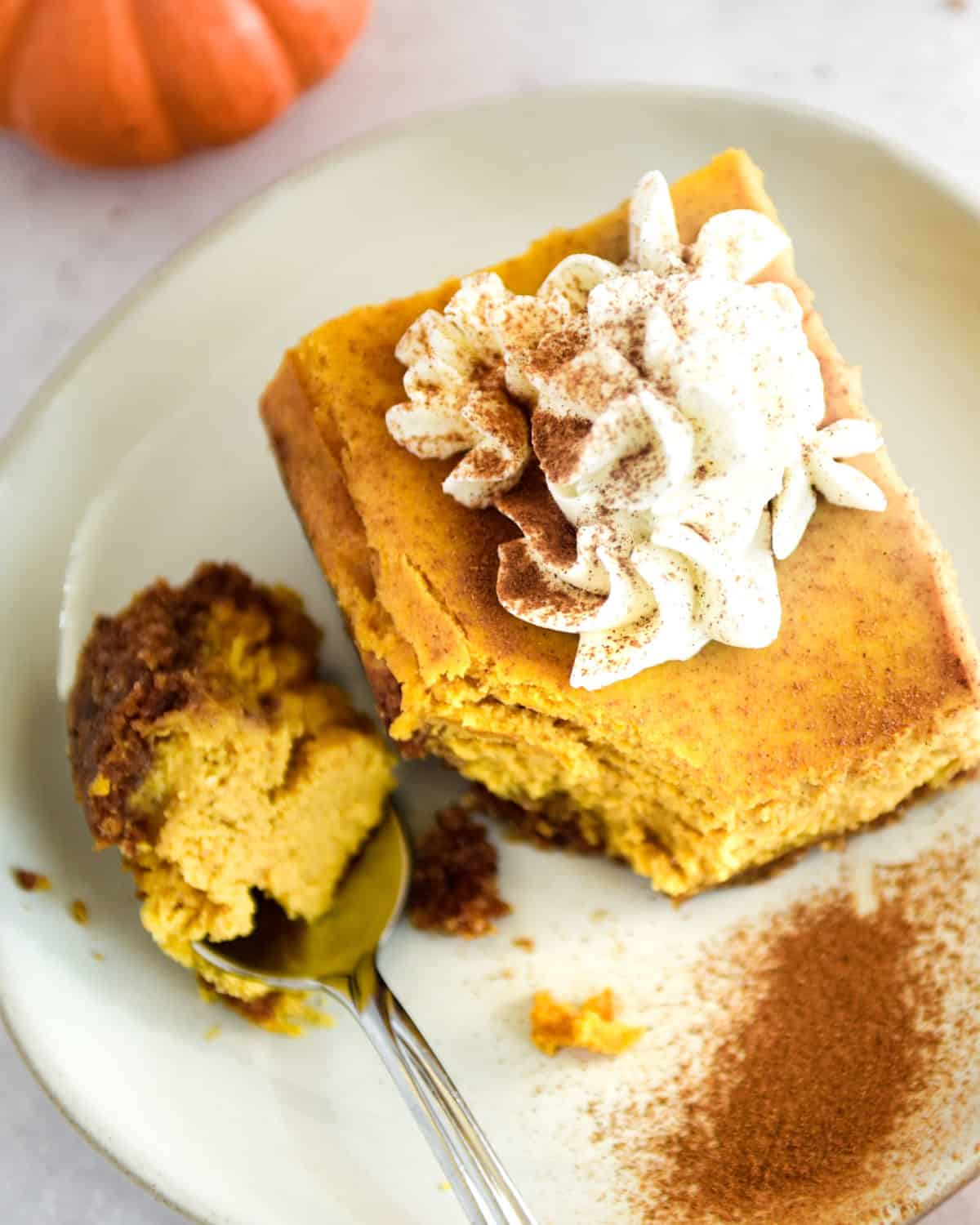 A close up of a pumpkin pie cheesecake bar topped with whipped cream and cinnamon.