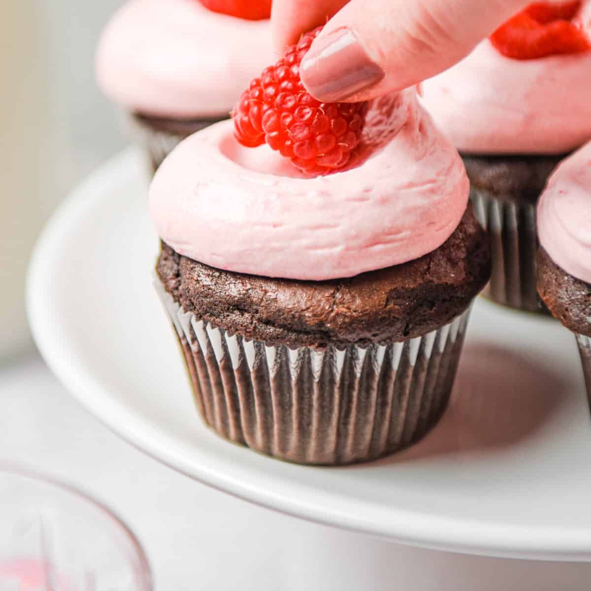 Placing a fresh raspberry on top of a chocolate cupcake.