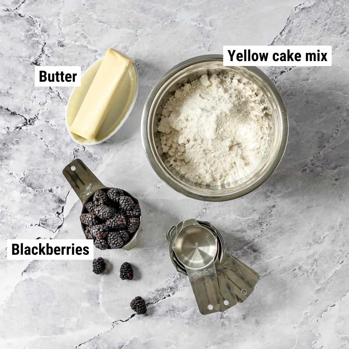 The ingredients to make blackberry cobbler with cake mix laid out on a table.