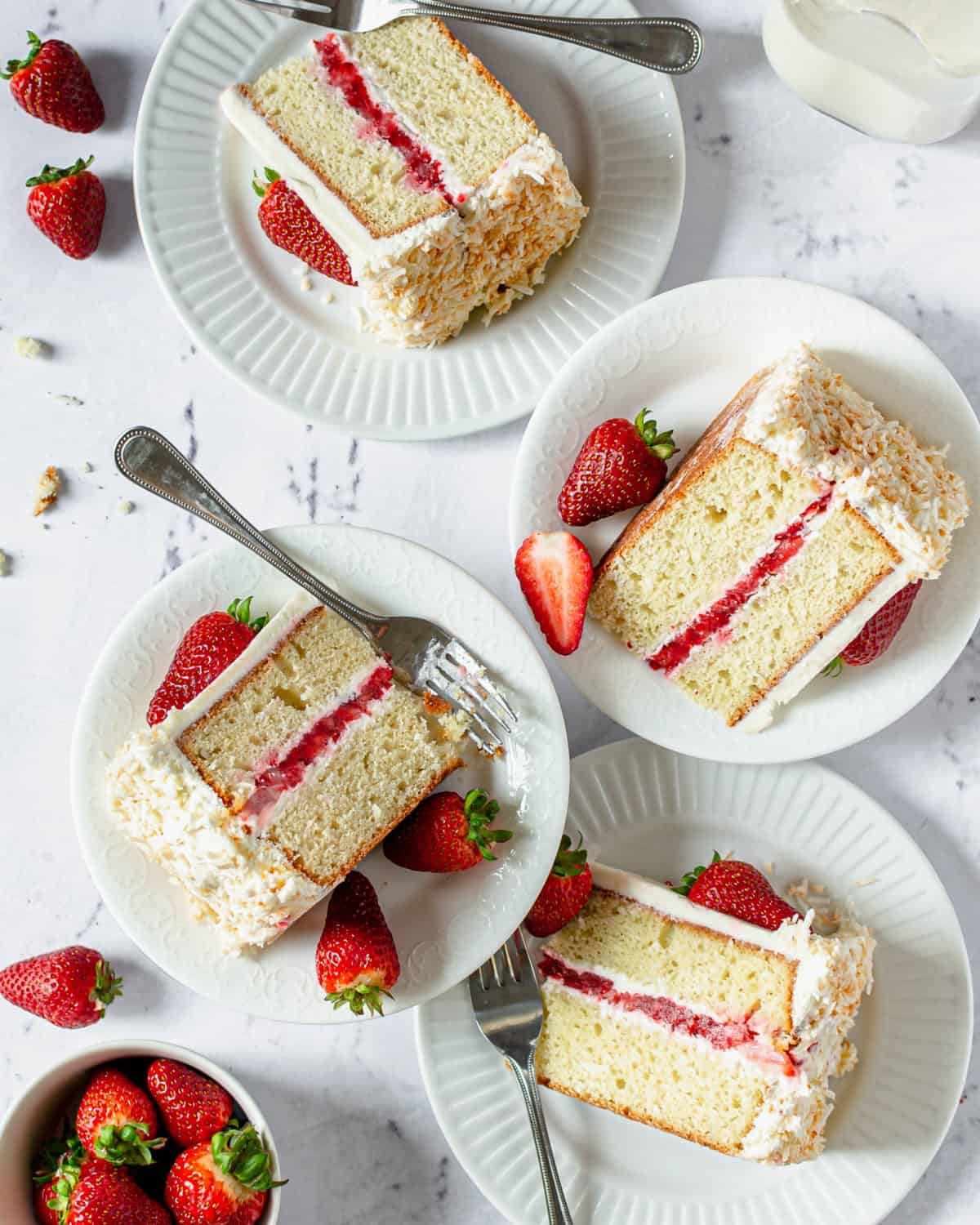 Four slices of coconut strawberry cake on plates with forks.