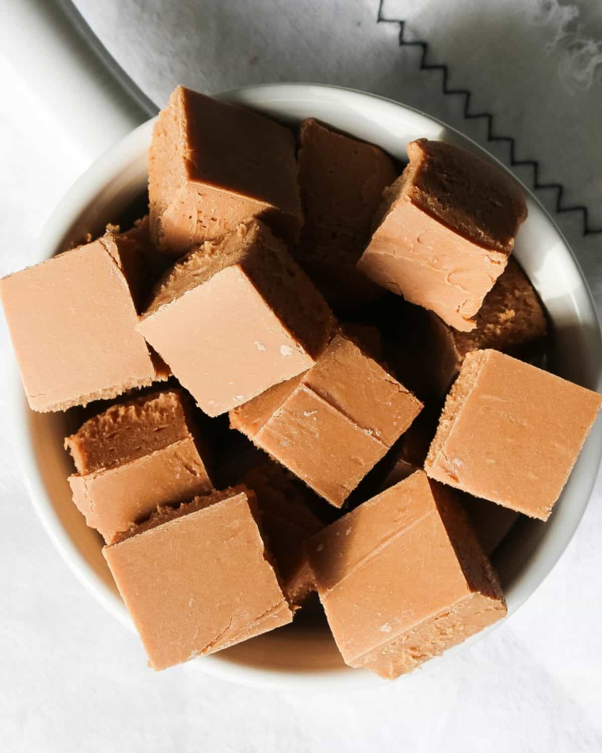 An overhead shot of squares of fudge in a white bowl.