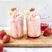 Two strawberry banana milkshakes on a table.