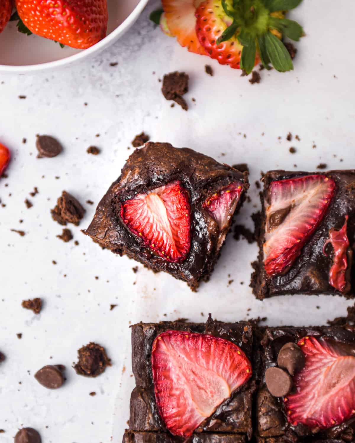 Brownies and strawberries surrounded with crumbs on a table.