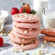 Several strawberry cake cookies stacked on top of each other with white chocolate chips scattered on a table.