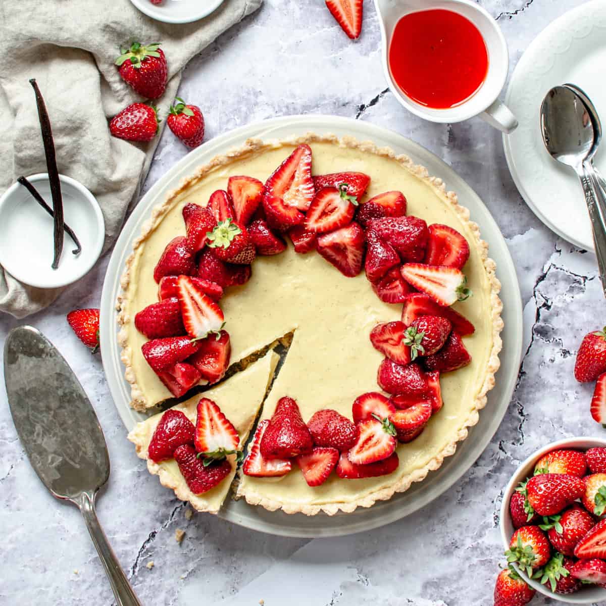 A finished strawberry custard tart on a plate with a serving knife.