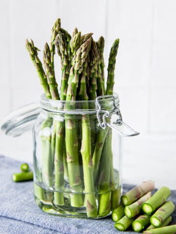 Asparagus in a jar of water on a blue kitchen cloth.