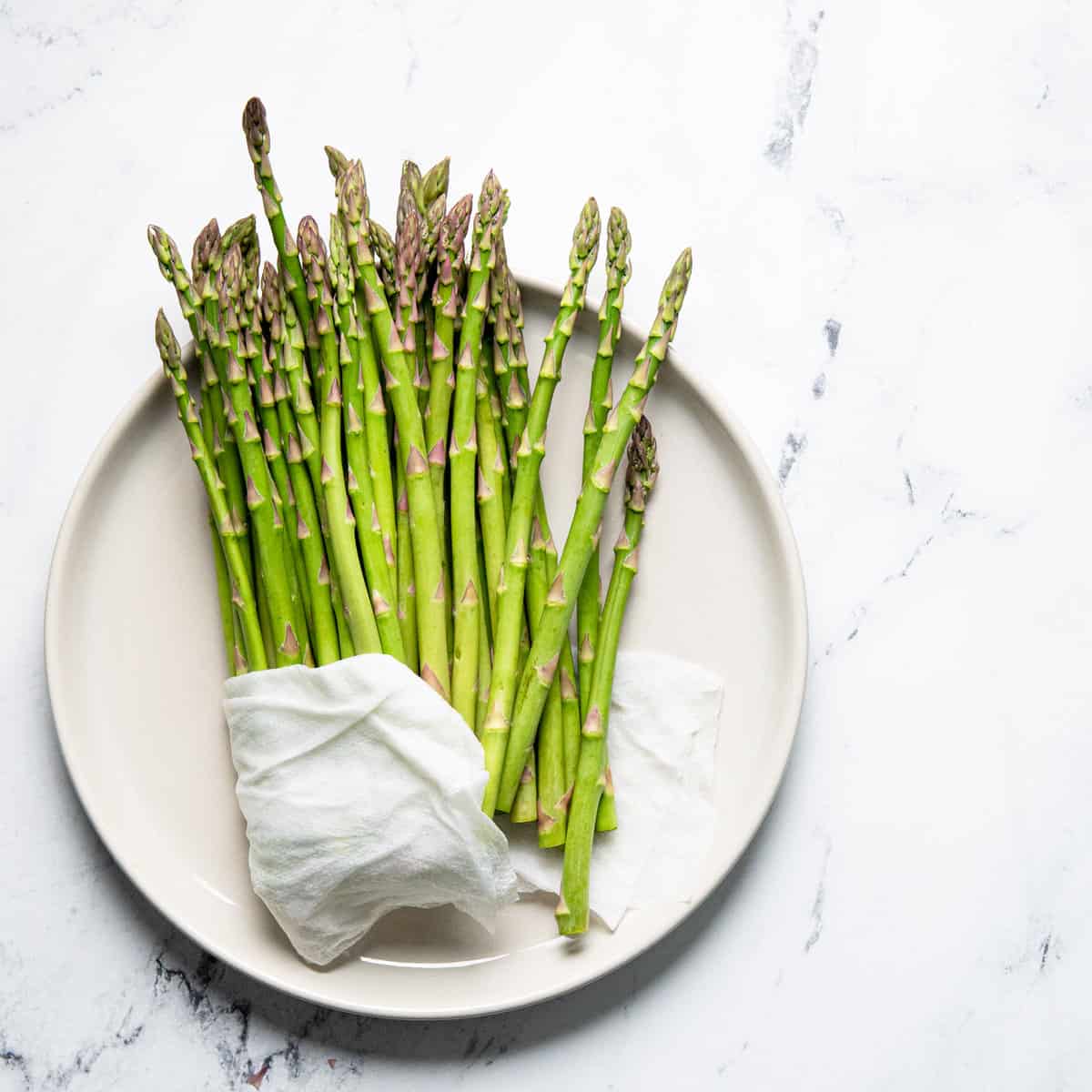 Asparagus in a wet towel on a white plate on a counter.