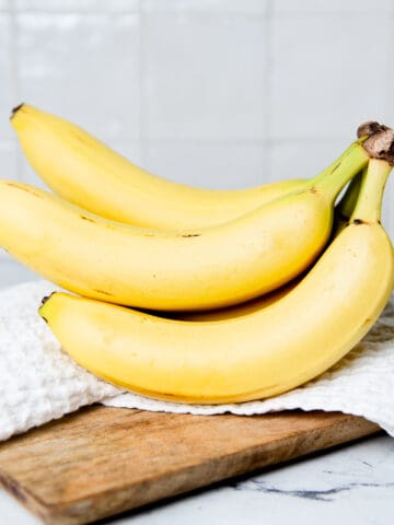 A bunch of bananas on a kitchen towel on a wooden breadboard.