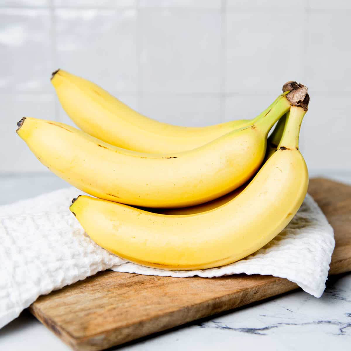 A bunch of bananas on a kitchen towel on a wooden breadboard.