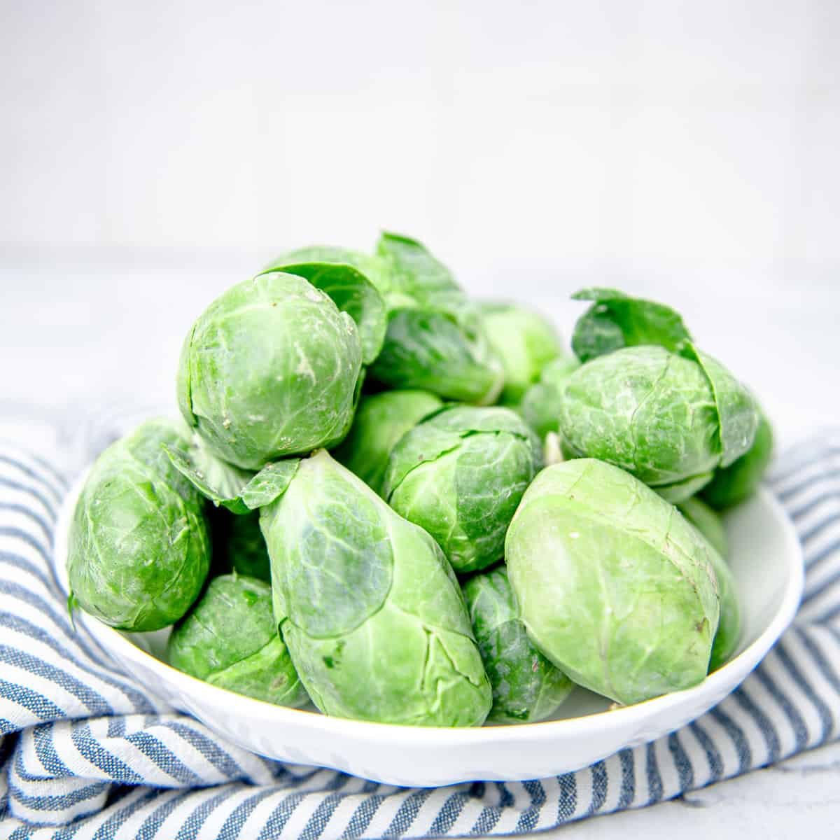 Brussel sprouts in white bowl with striped napkin.
