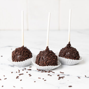 Three cake pops on a kitchen counter with sprinkles.