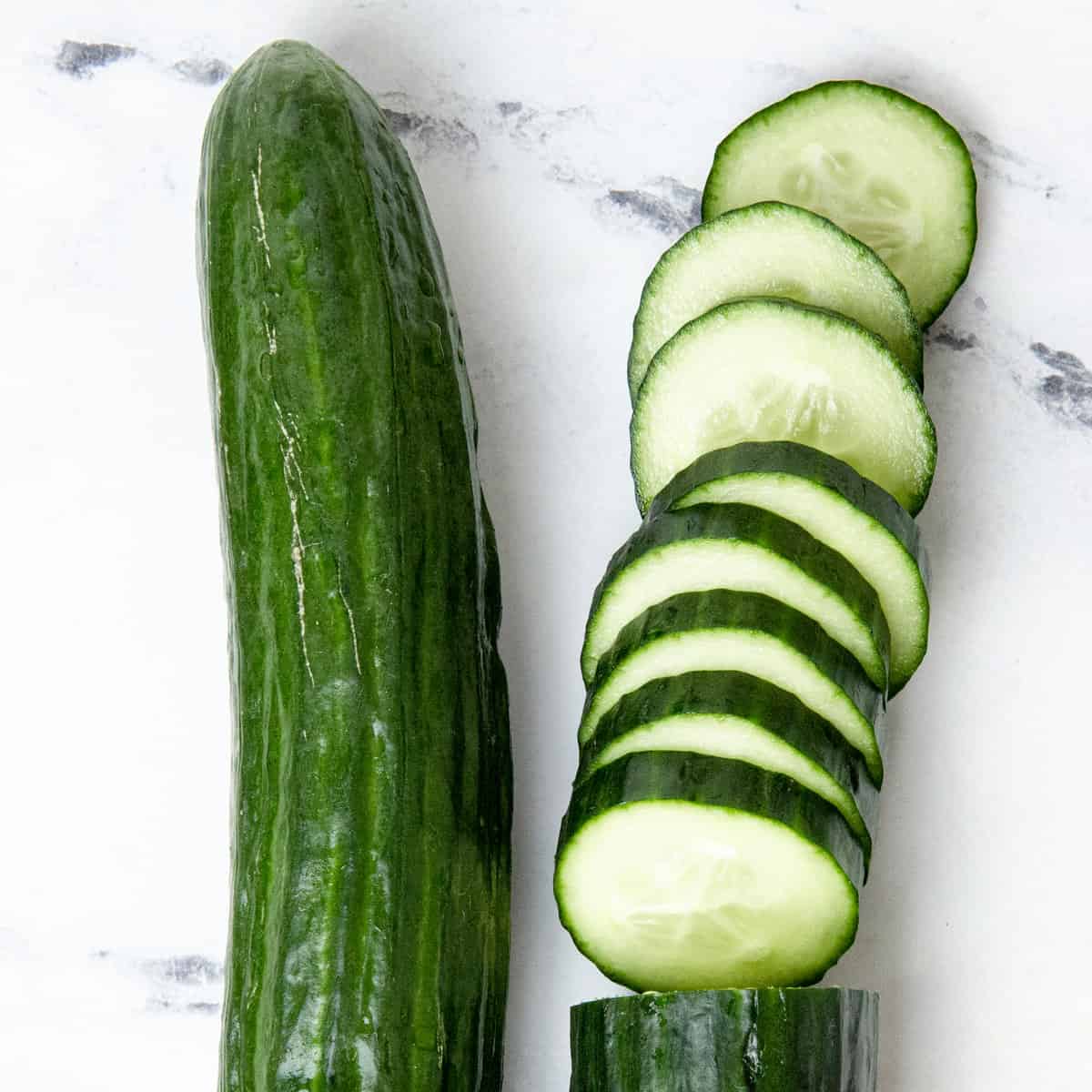 Cucumbers sliced on a kitchen counter, with an uncut cucumber next to it.