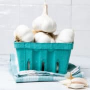 Garlic bulbs in a blue container on top of a blue and white kitchen towel.