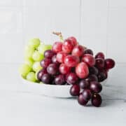 Green and red grapes in a white bowl.