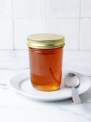 Honey in a clear jar on a white plate with a spoon.