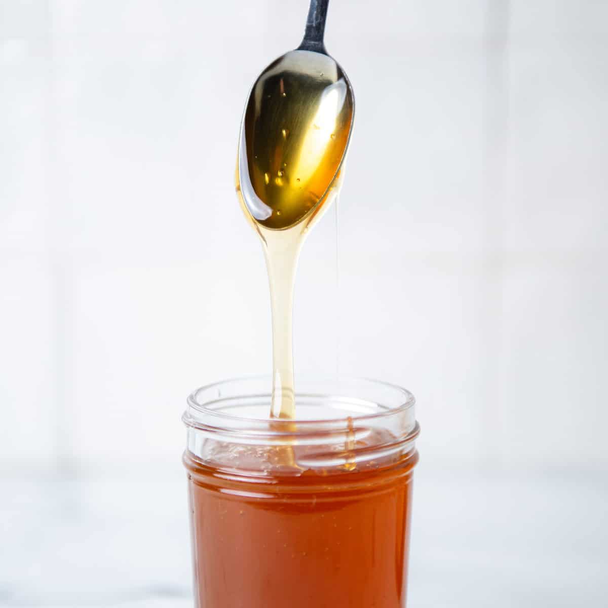 Honey dripping off a spoon into a honey jar.