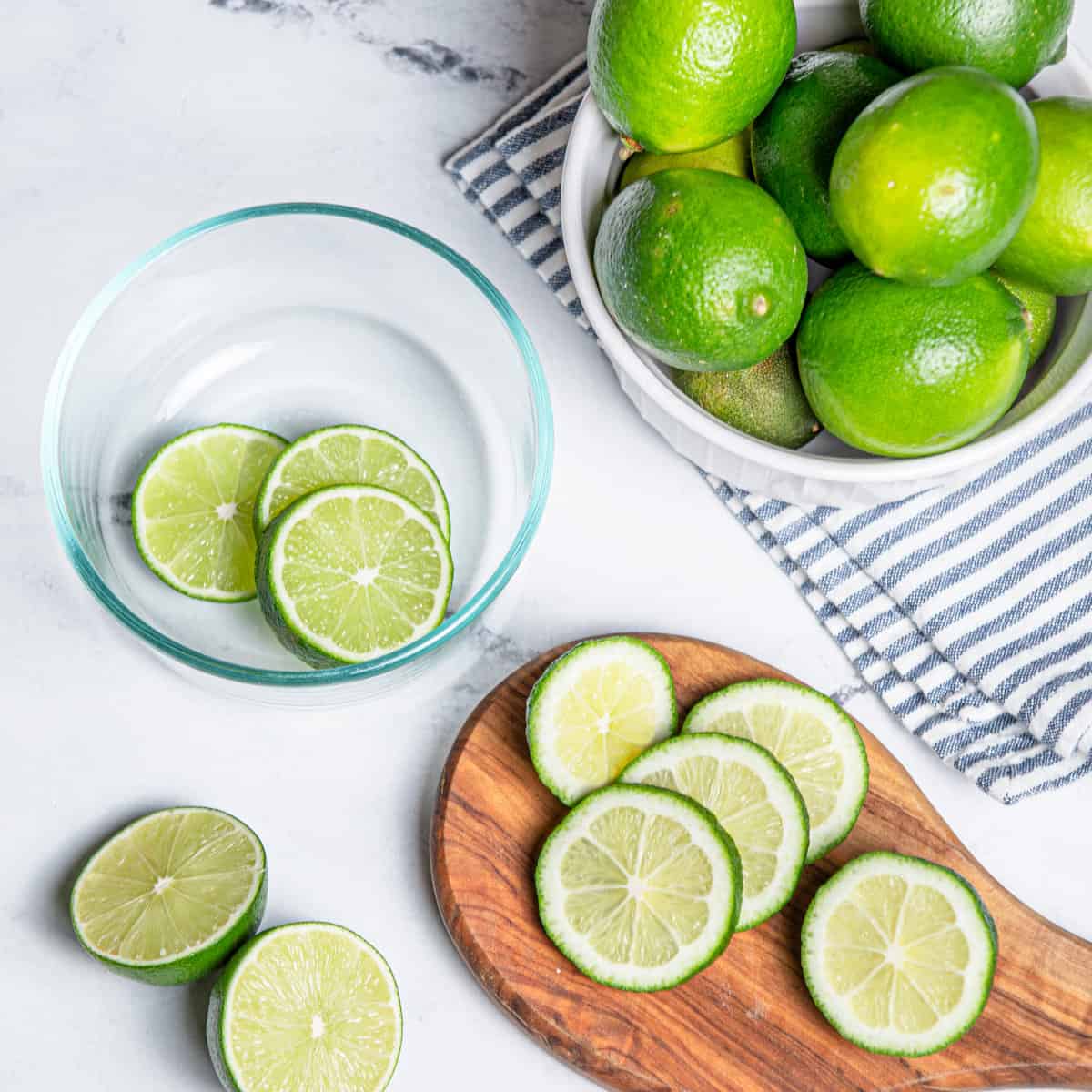 Limes being sliced on a wooden chopping board.