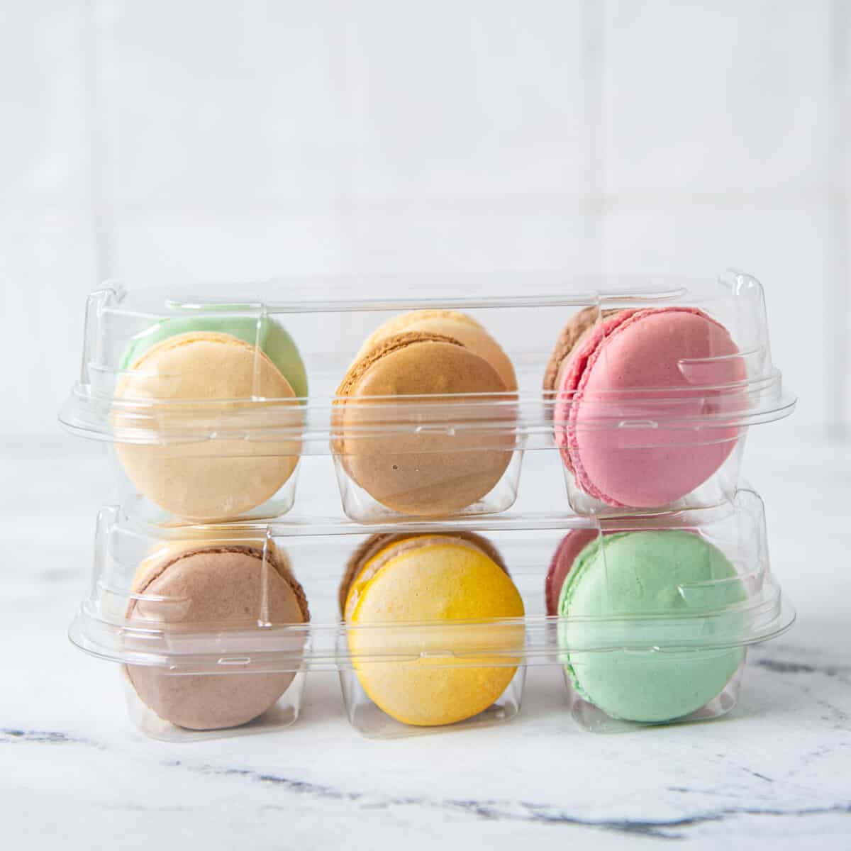 A variety of colored macarons packaged in two clear containers.