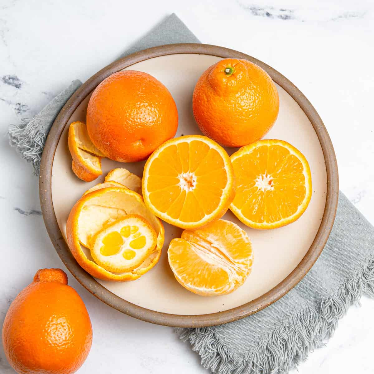 Sliced and unsliced oranges in a plate on a kitchen towel.