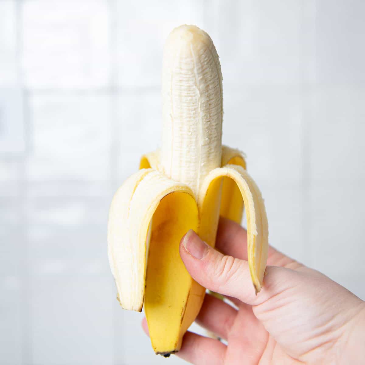 A peeled banana is being held by a hand.