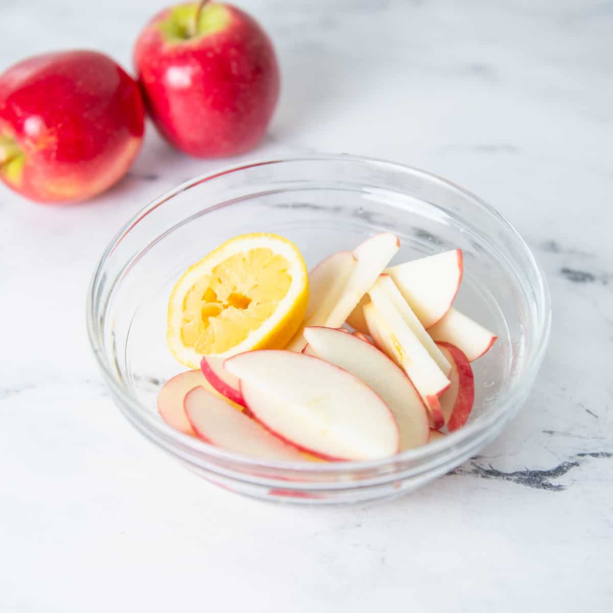 Sliced apples in a clear class bowl with lemon juice.
