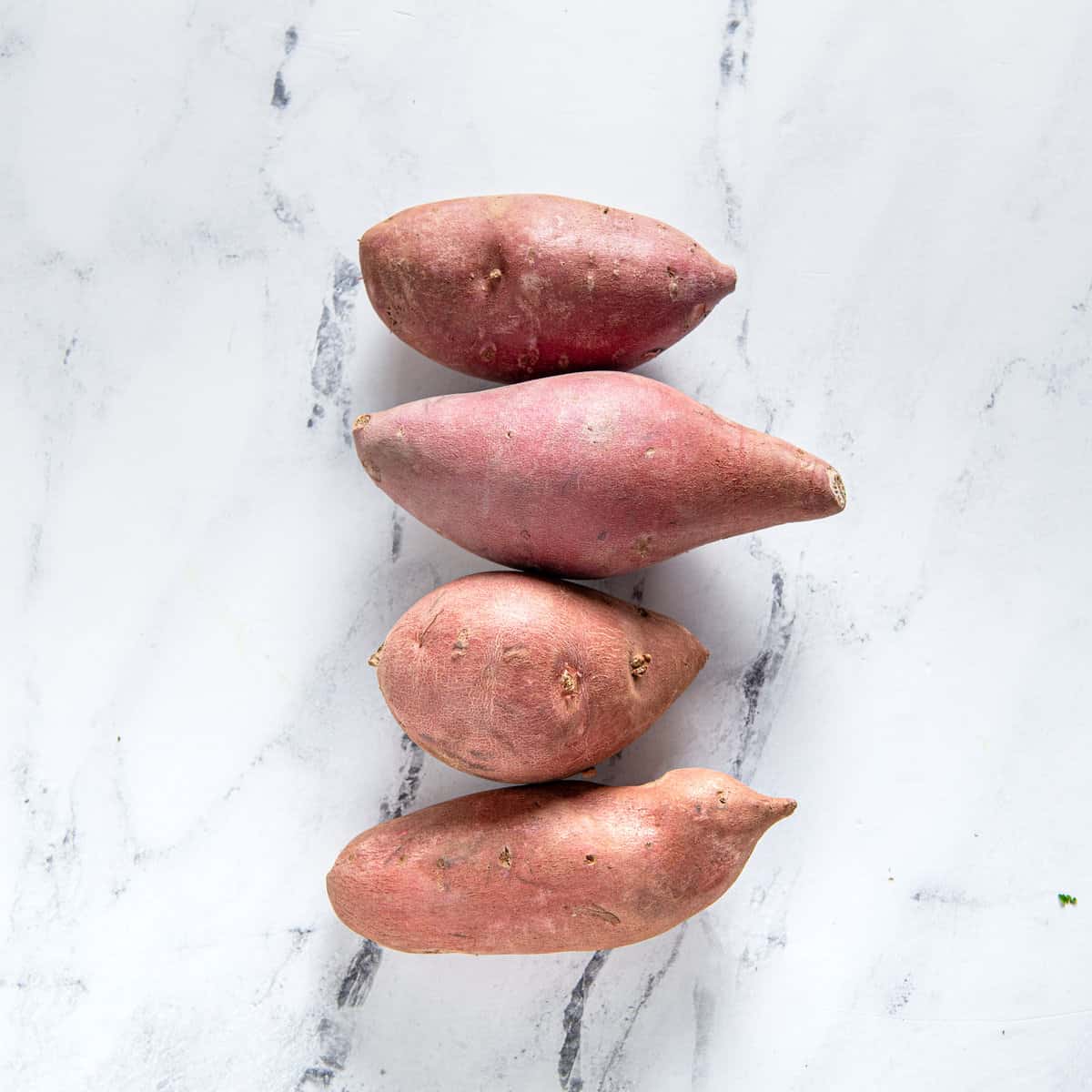 Four sweet potatoes on a kitchen counter.