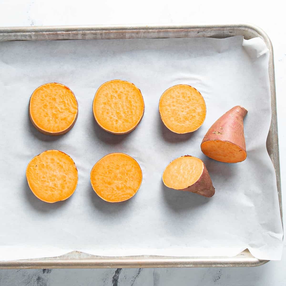 Sweet potato rounds on parchment paper on a baking tray.